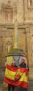 Foto del rosario realizado en Murcia de la ctc. Hombre y mujer sosteniendo una bandera de España con el sagrado corazón de jesús delante de una cruz de piedra dentro de una Iglesia.